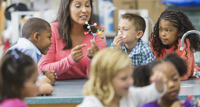Multiracial teacher and children in science lab An Hispanic woman in her 40s teaching a multi-ethnic group of elementary school students in science lab. She is holding a model of a molecule and talking while the curious children watch and listen.